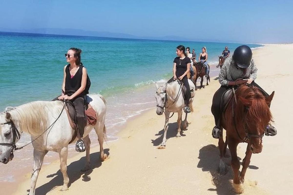 un grup de persones muntant a cavall a la platja