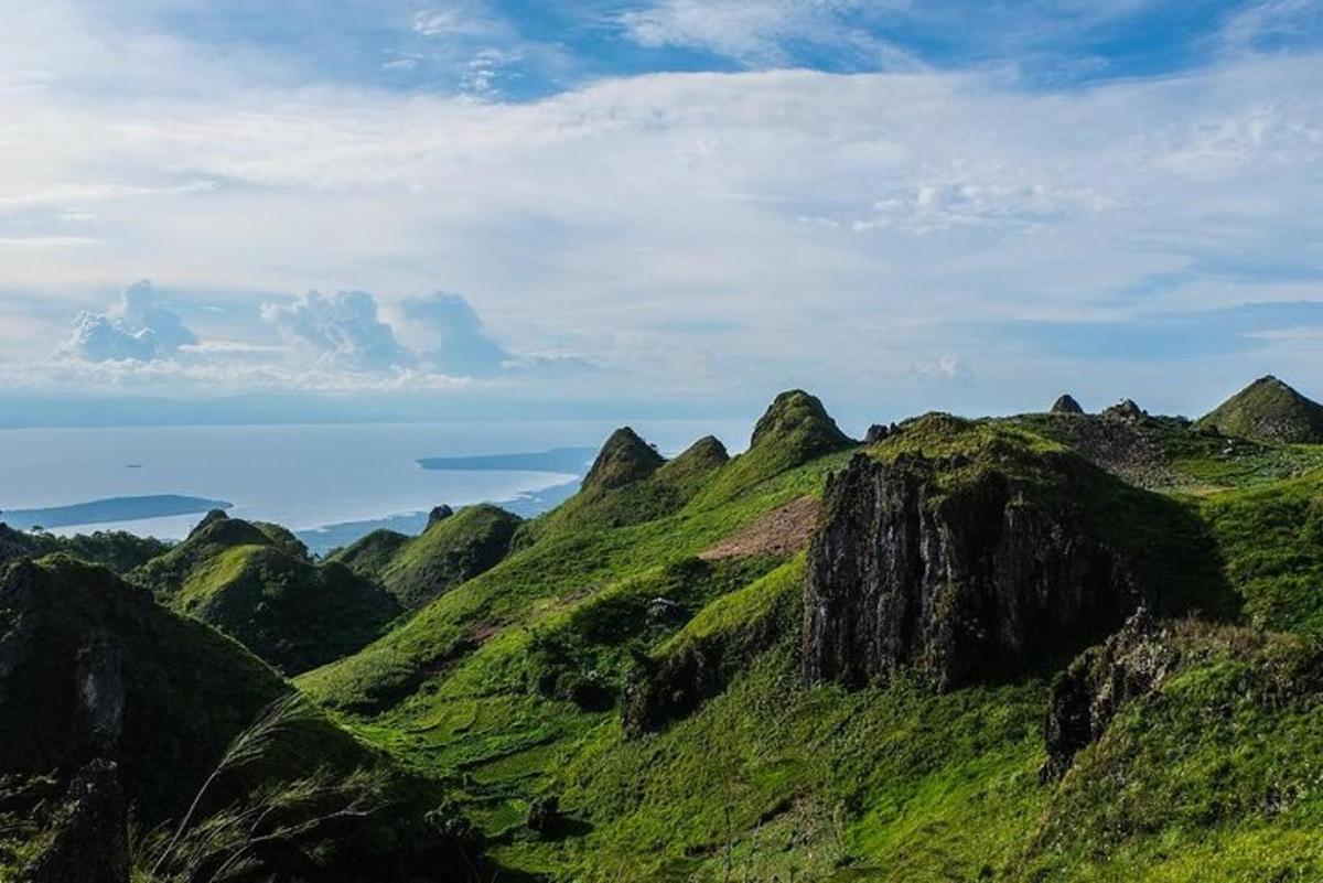 a green hill with rocks and the ocean in the background