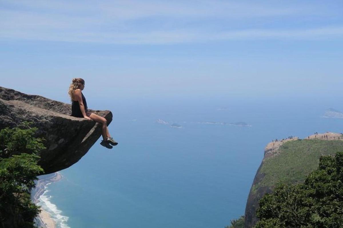 uma mulher sentada em um penhasco com vista para o oceano
