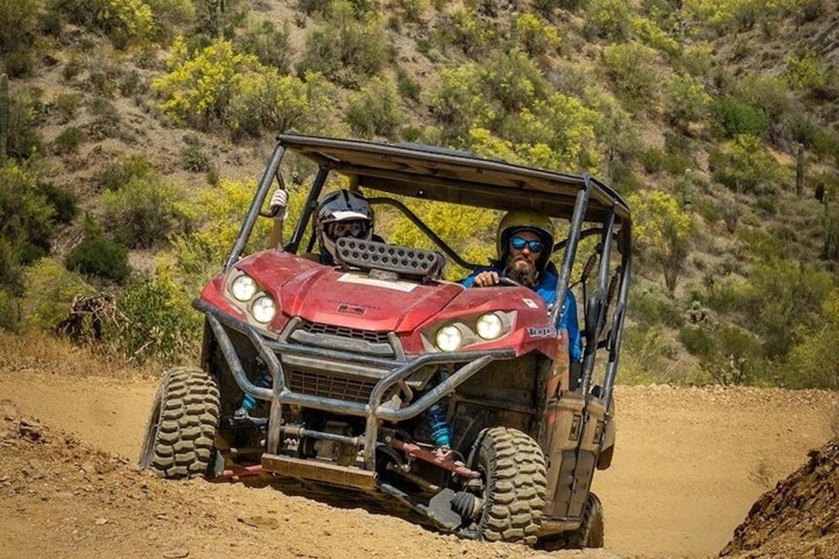 Dos personas viajando en un vehículo todo terreno rojo por un camino de tierra.