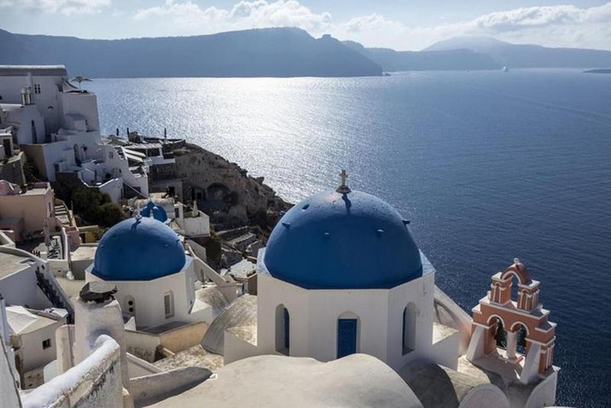 um grupo de edifícios brancos com cúpulas azuis e o oceano