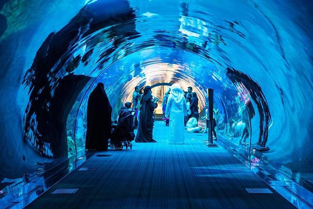 a group of people walking through a tunnel with an aquarium