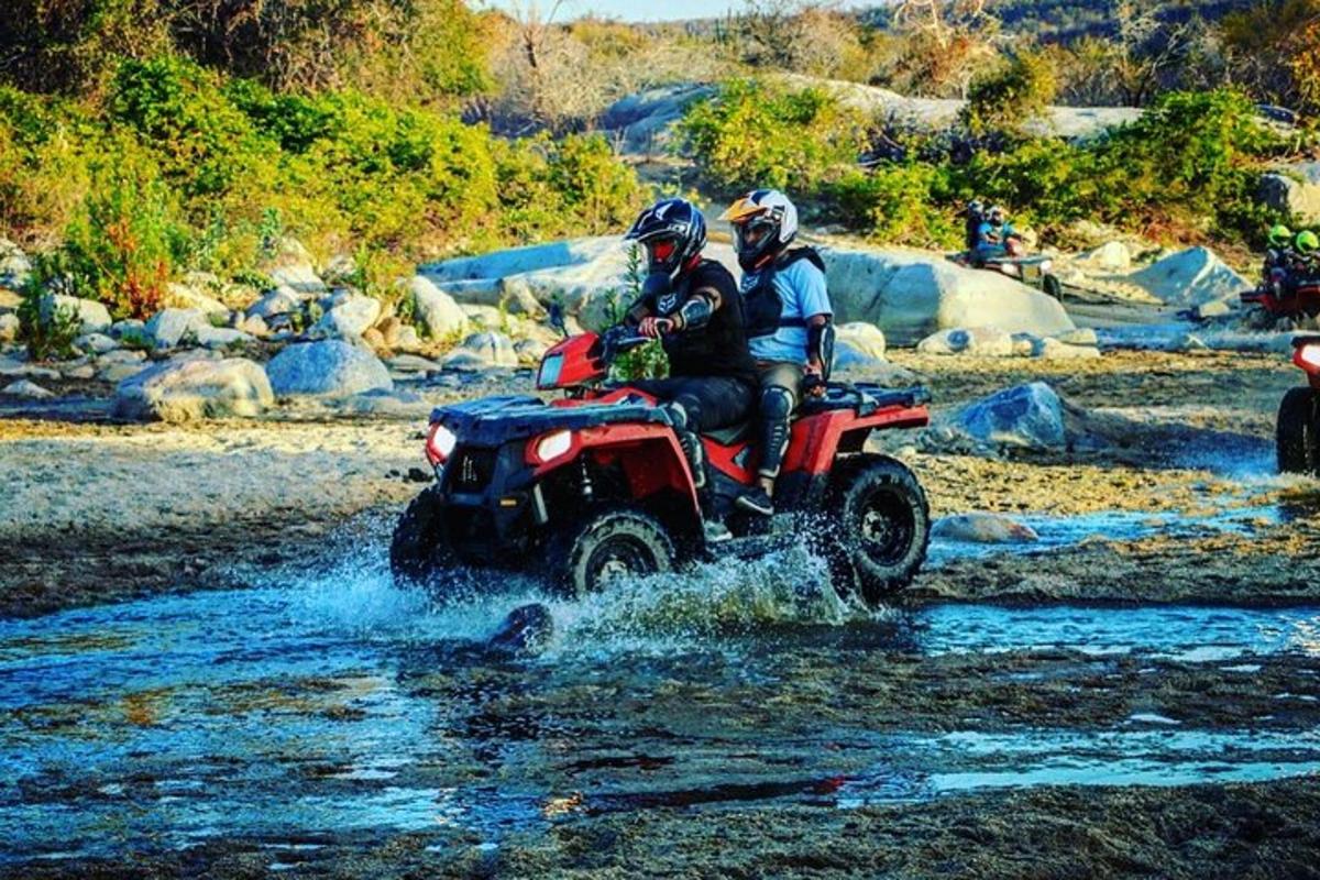 two people riding on a four wheeler through a river