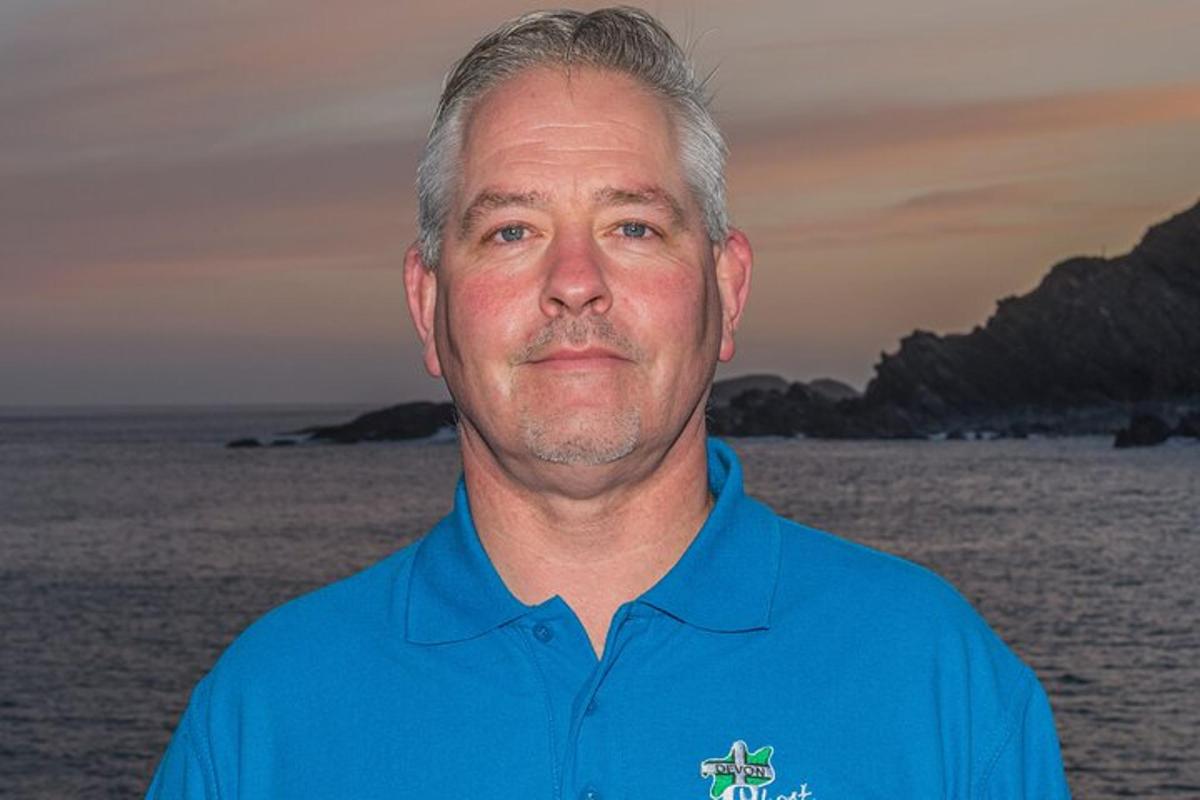 a man in a blue shirt standing in front of the ocean