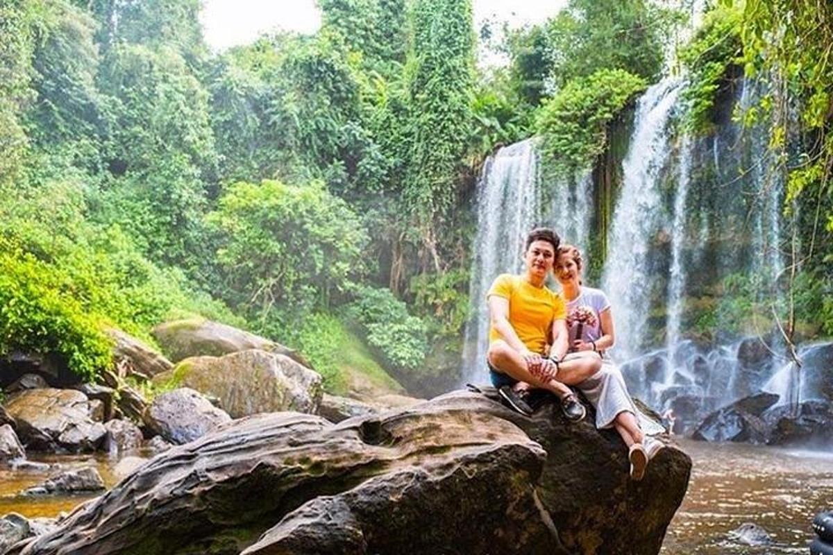 un uomo e una donna seduti su una roccia di fronte a una cascata