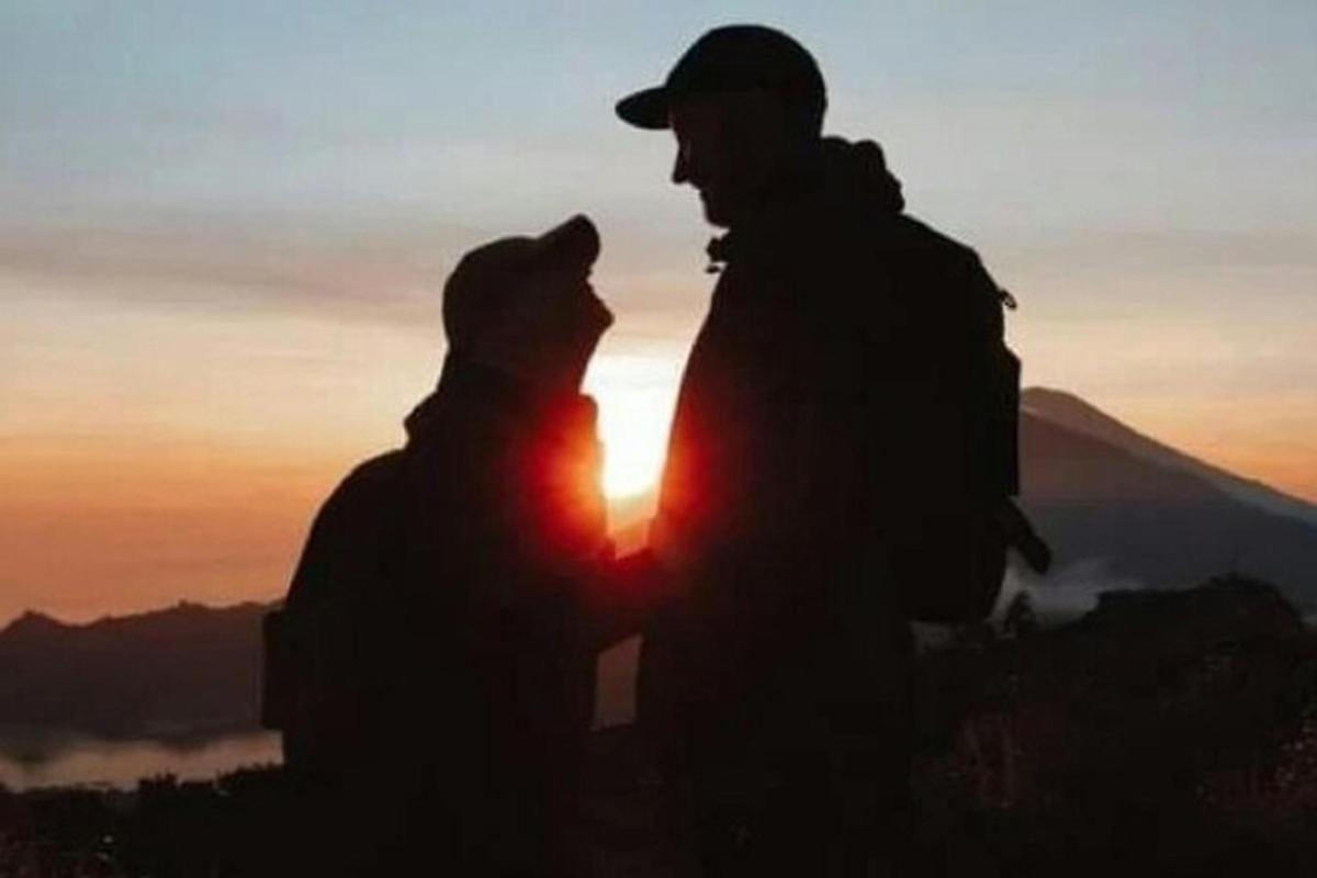 zwei Menschen sitzen bei Sonnenuntergang auf einem Berggipfel