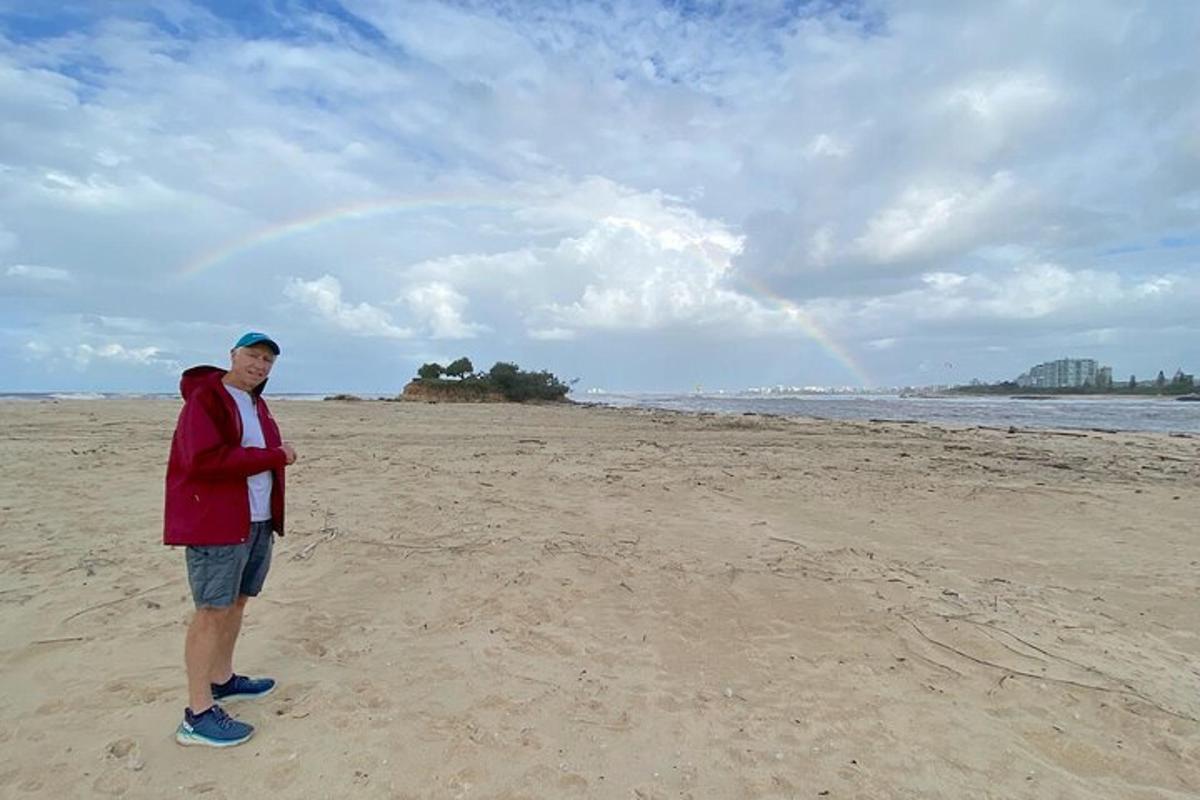 a man standing on a beach with a rainbow in the background