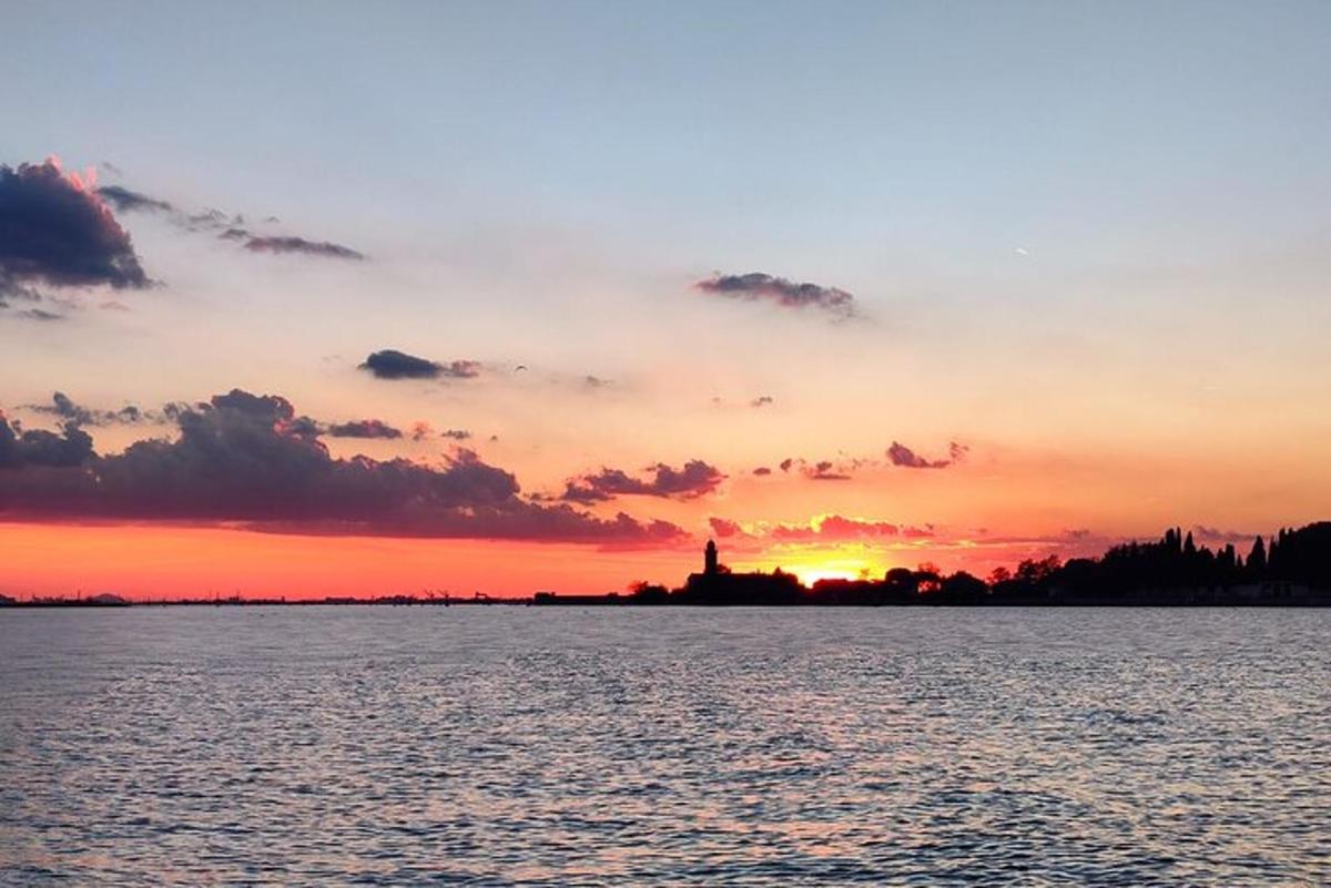 una posta de sol sobre l'aigua amb un far a la distància
