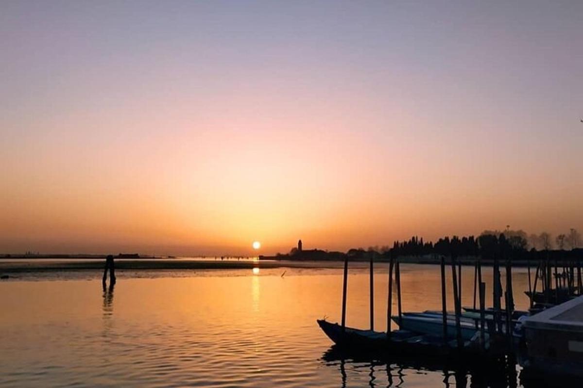 un uomo in piedi nell'acqua mentre il sole tramonta