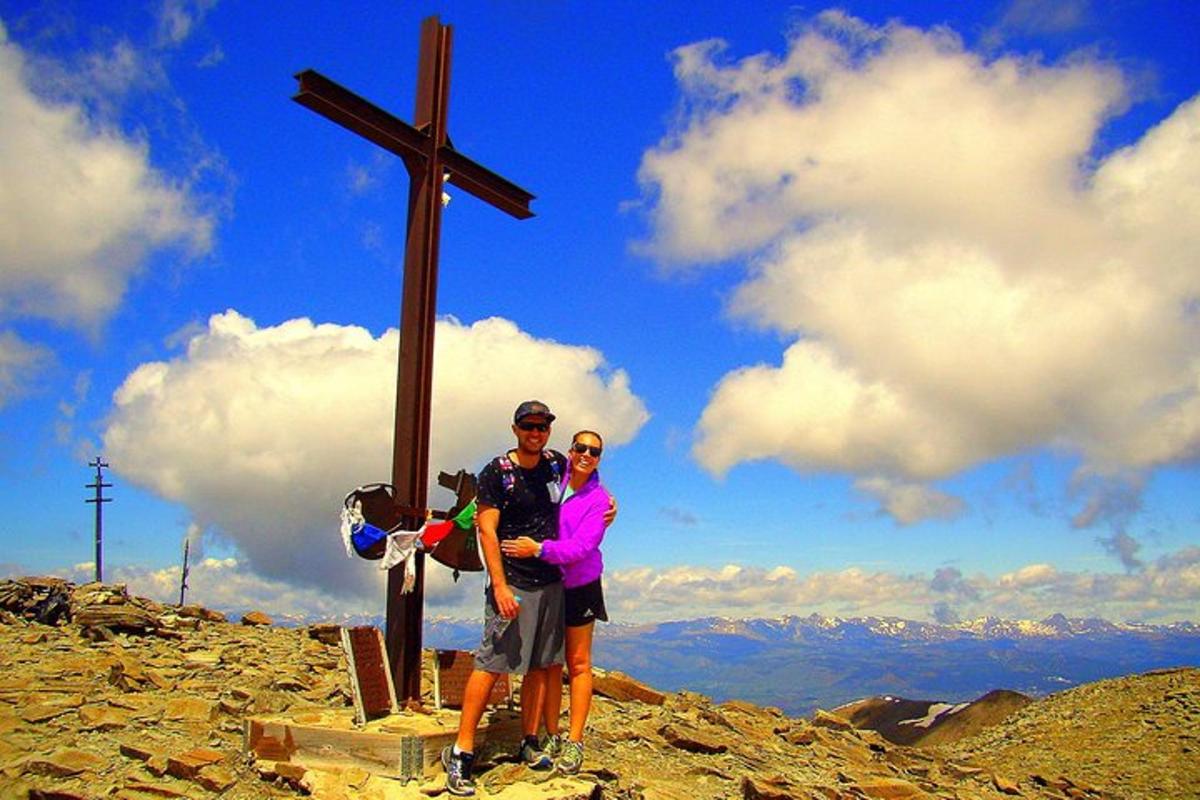 a man and woman standing next to a cross on a mountain