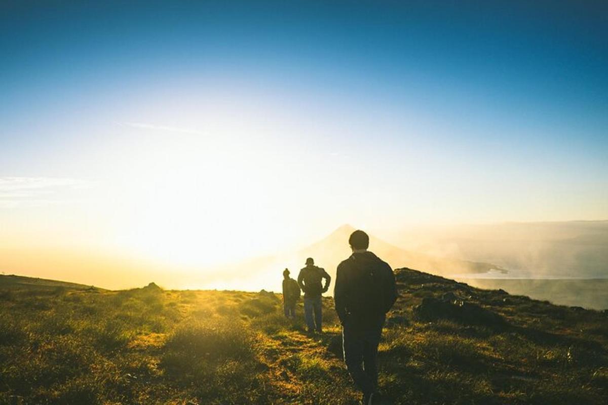 drei Personen stehen auf einem Hügel und schauen auf den Sonnenaufgang