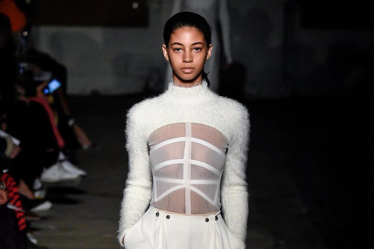 una donna che cammina su una passerella indossando un maglione bianco