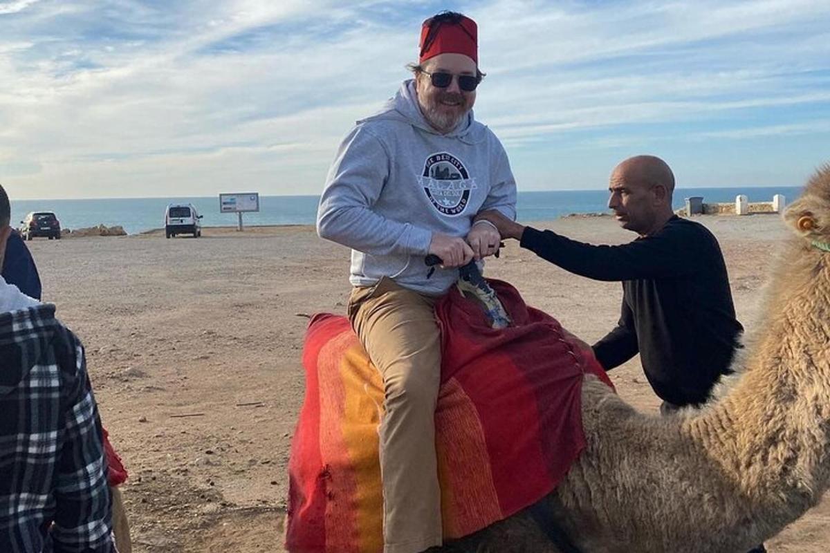 en mann som sitter på en kamel på stranden