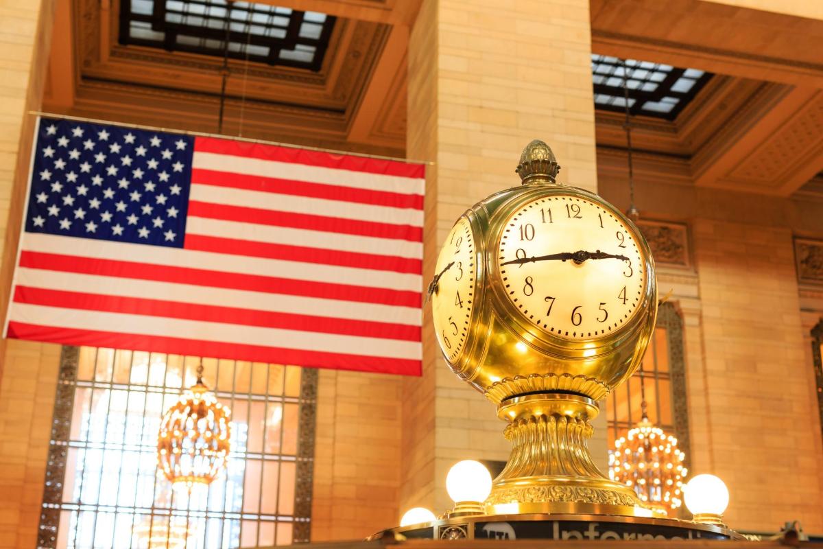 a gold clock in front of an american flag