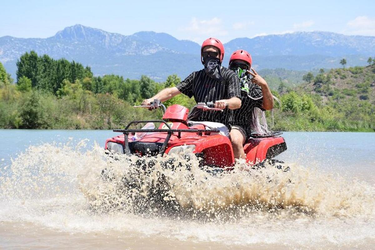dva lidé jedoucí na čtyřkolce ve vodě