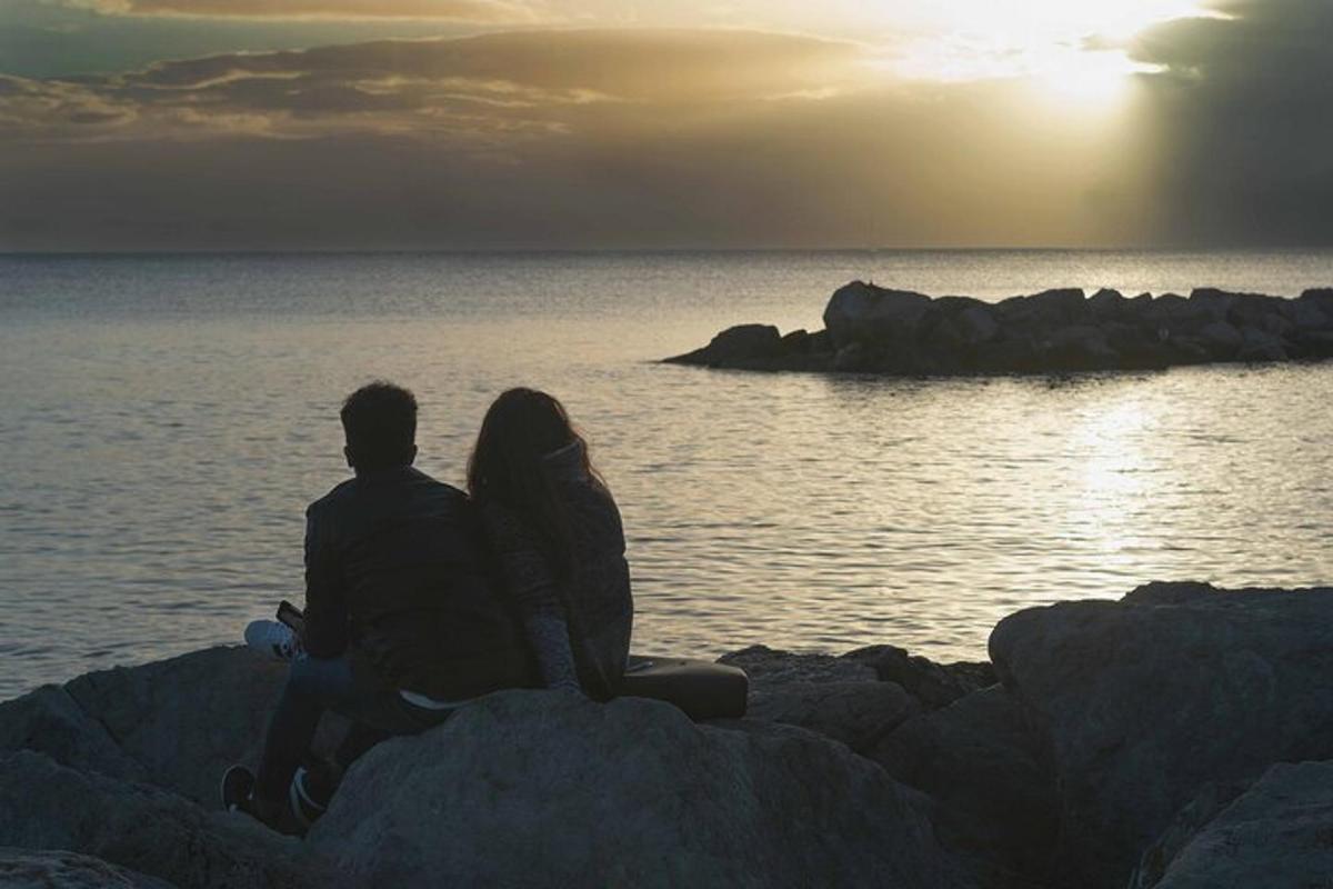 a man and a woman sitting on rocks near the water
