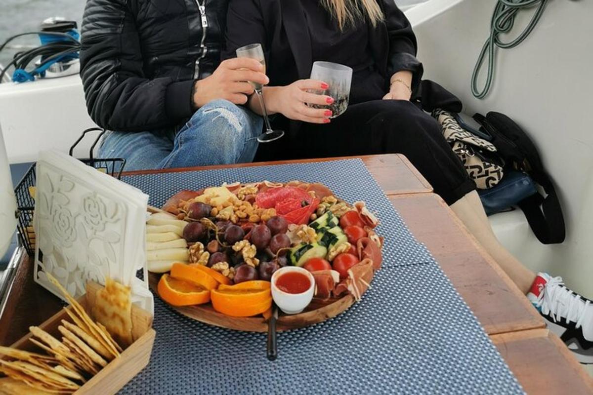 uz galda šķīvis ar ēdienu, divi cilvēki tur rokās dzērienus