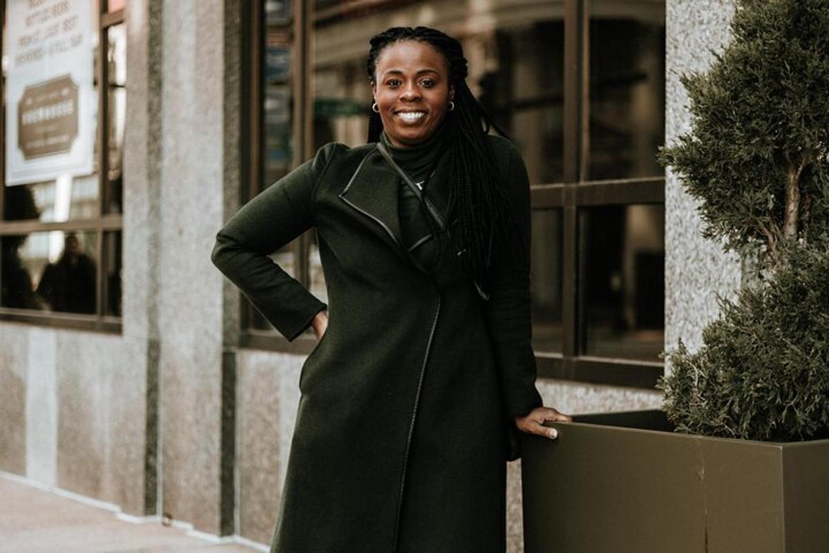 a woman in a green coat standing next to a potted plant