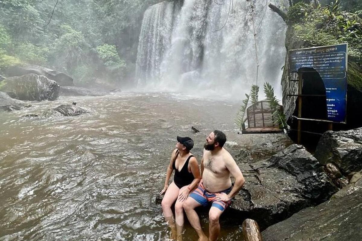 Ein Mann und eine Frau sitzen im Wasser in der Nähe eines Wasserfalls