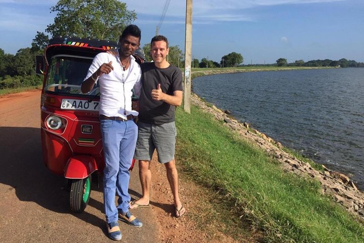 dois homens parados ao lado de um carro vermelho próximo a um corpo d'água