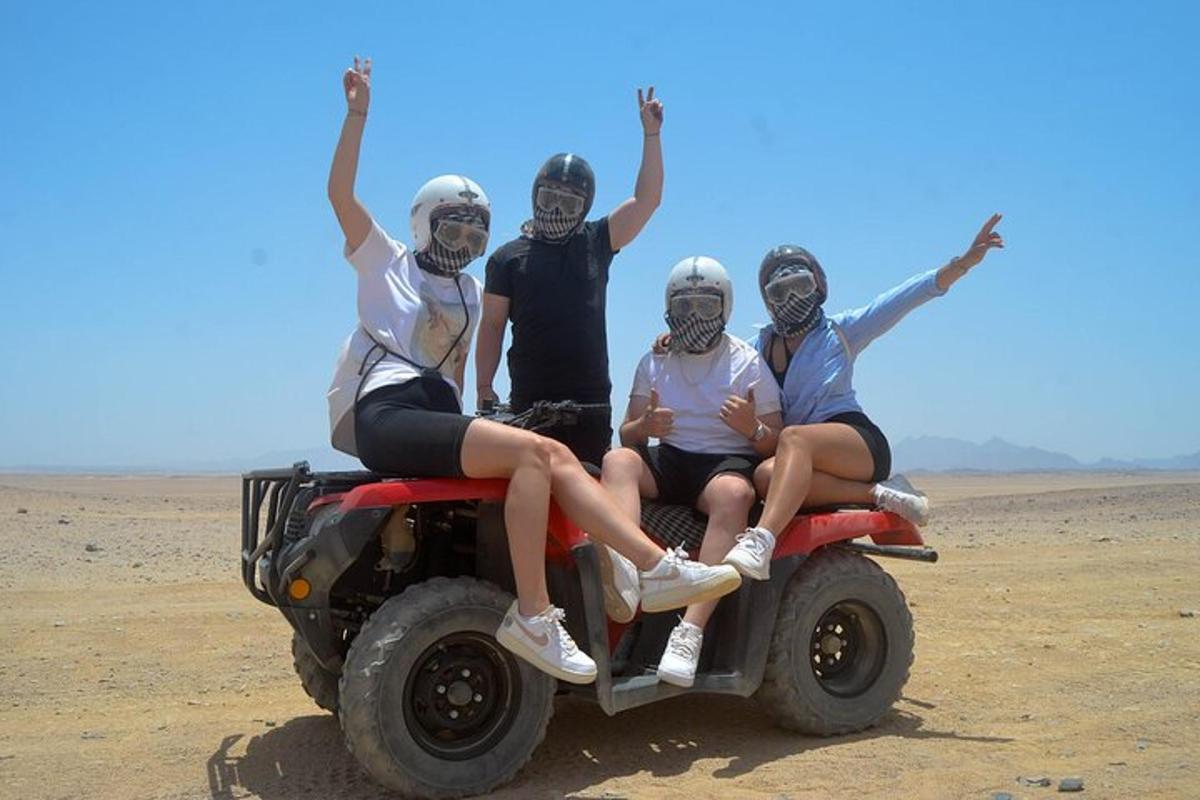 four people sitting on the back of a four wheeler in the desert