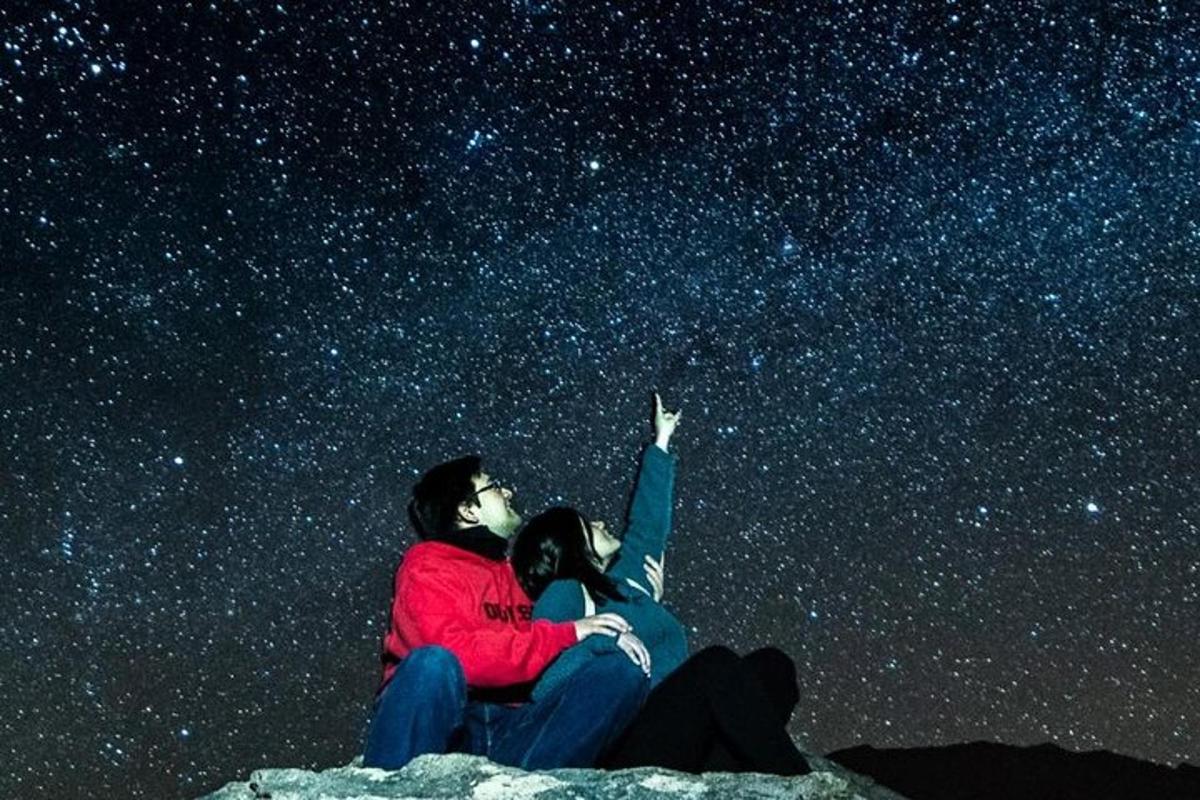 a couple sitting on a rock looking up at the stars