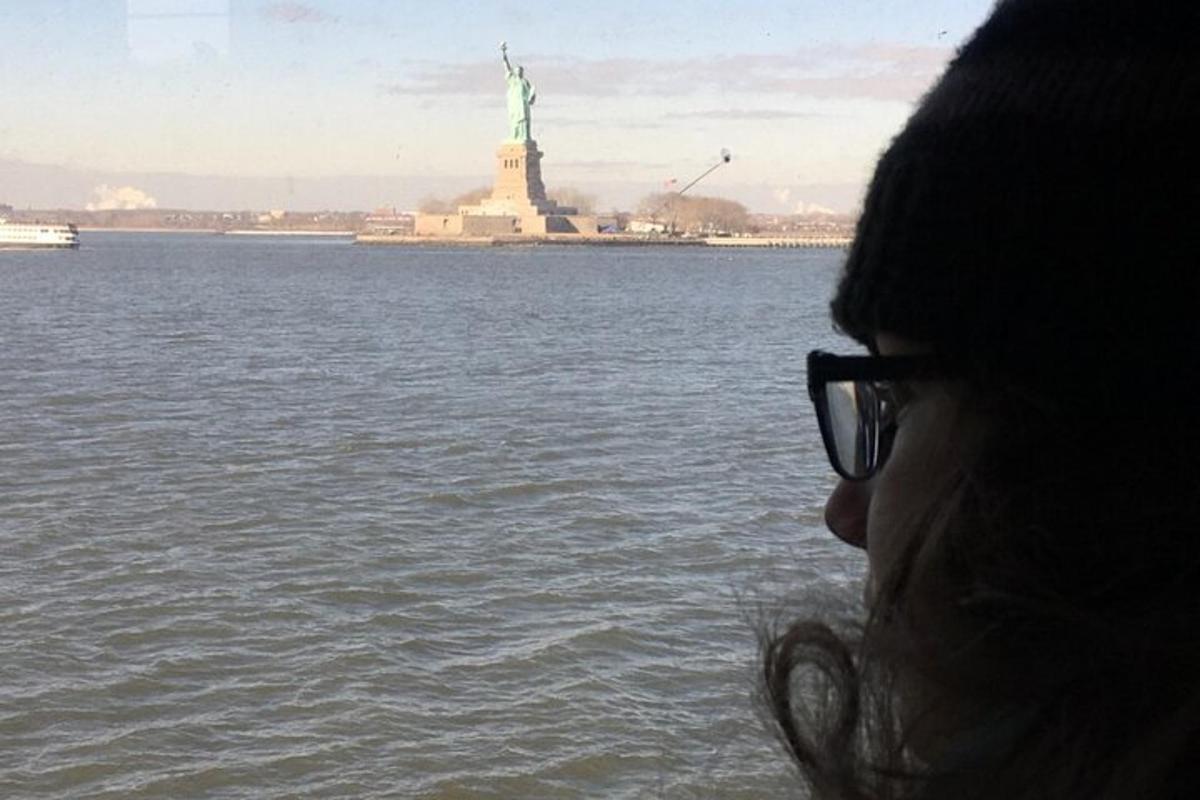 a woman wearing glasses looking at the statue of liberty