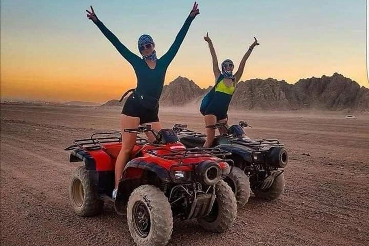 two women are standing on atvs in the desert