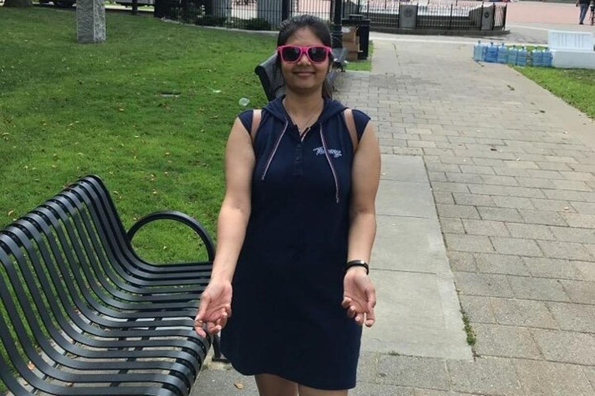 een vrouw in een zwarte jurk die naast een bankje staat