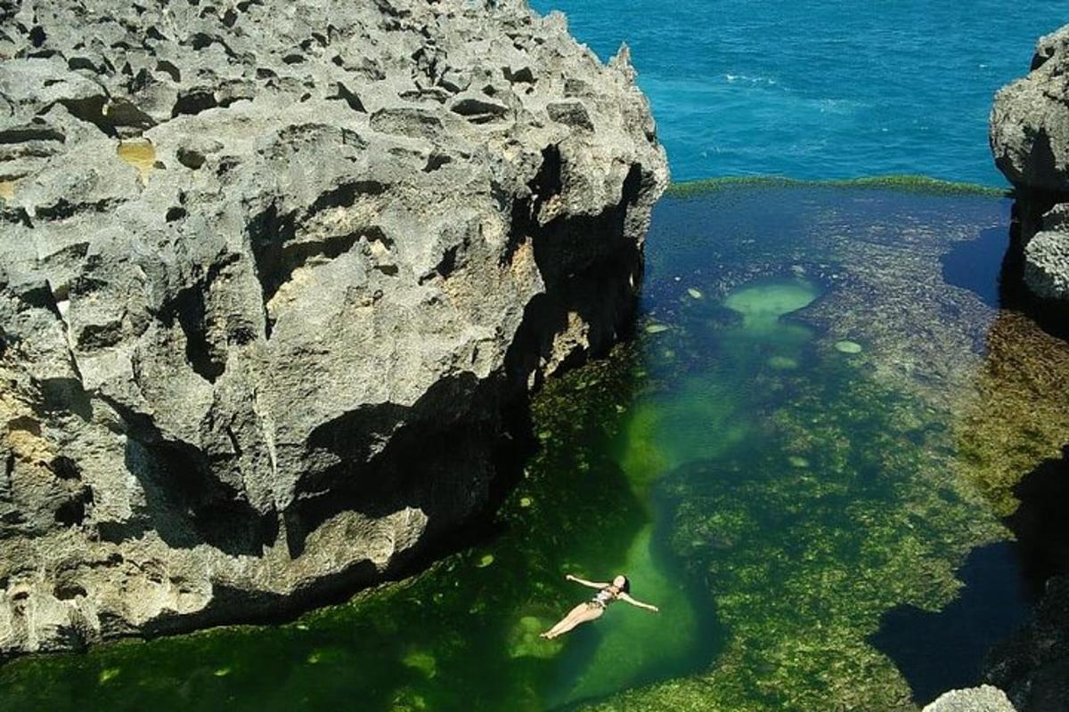 osoba plavající ve vodní ploše vedle útesu