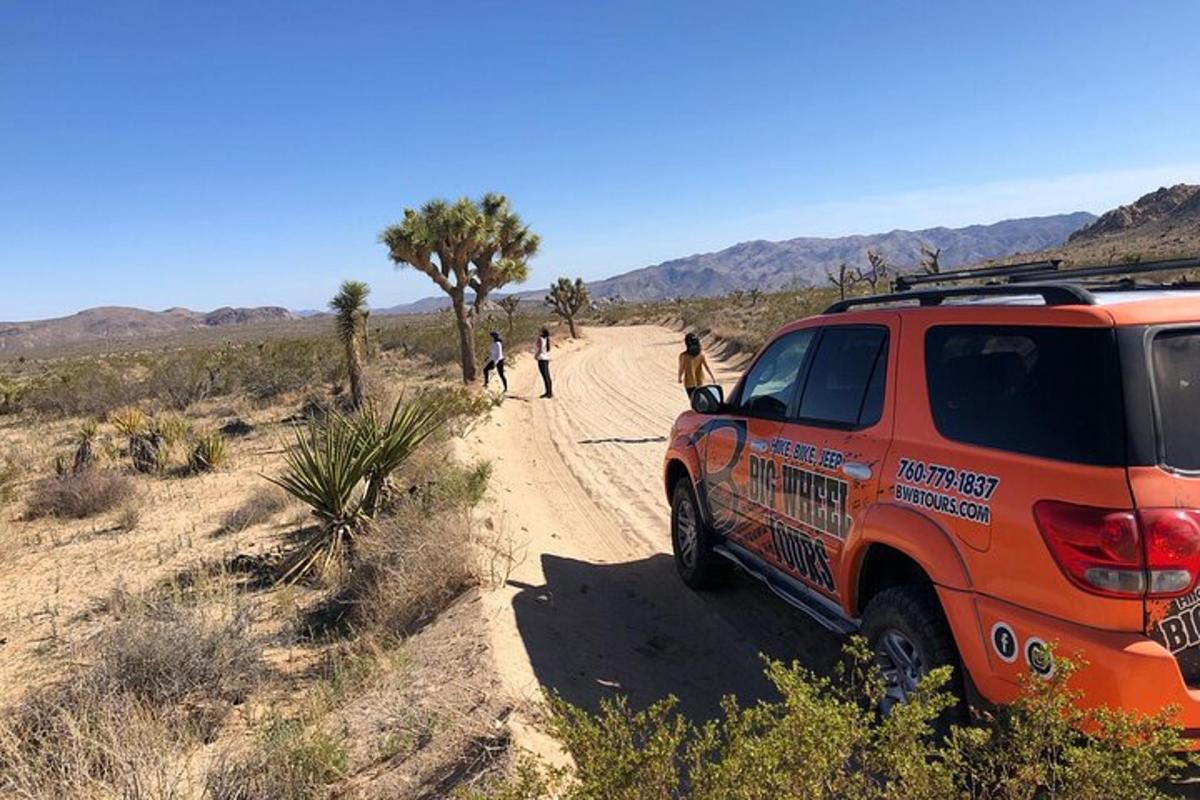 Un camión naranja estacionado en un camino de tierra en el desierto.
