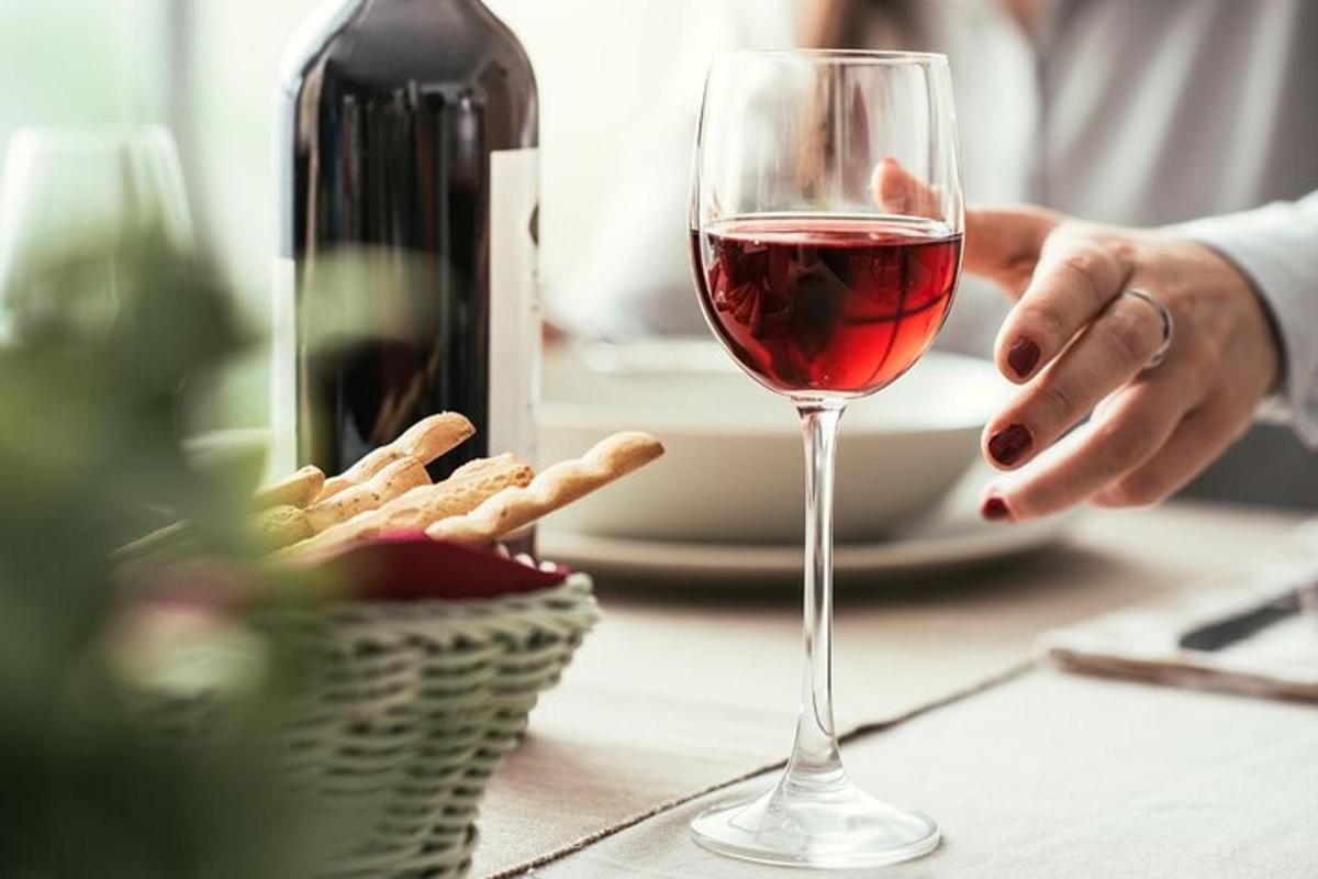 una persona sosteniendo una copa de vino junto a una canasta de comida