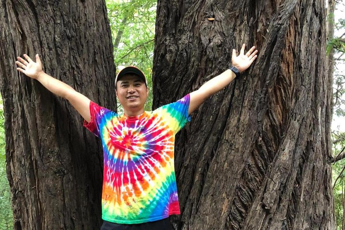Un hombre con una camisa teñida de pie junto a un árbol.