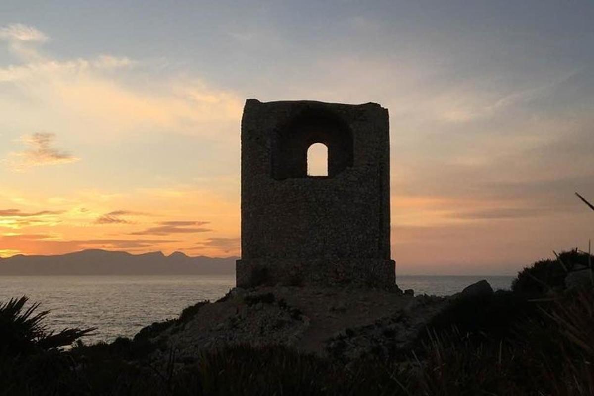 a stone tower on the shore of the ocean at sunset