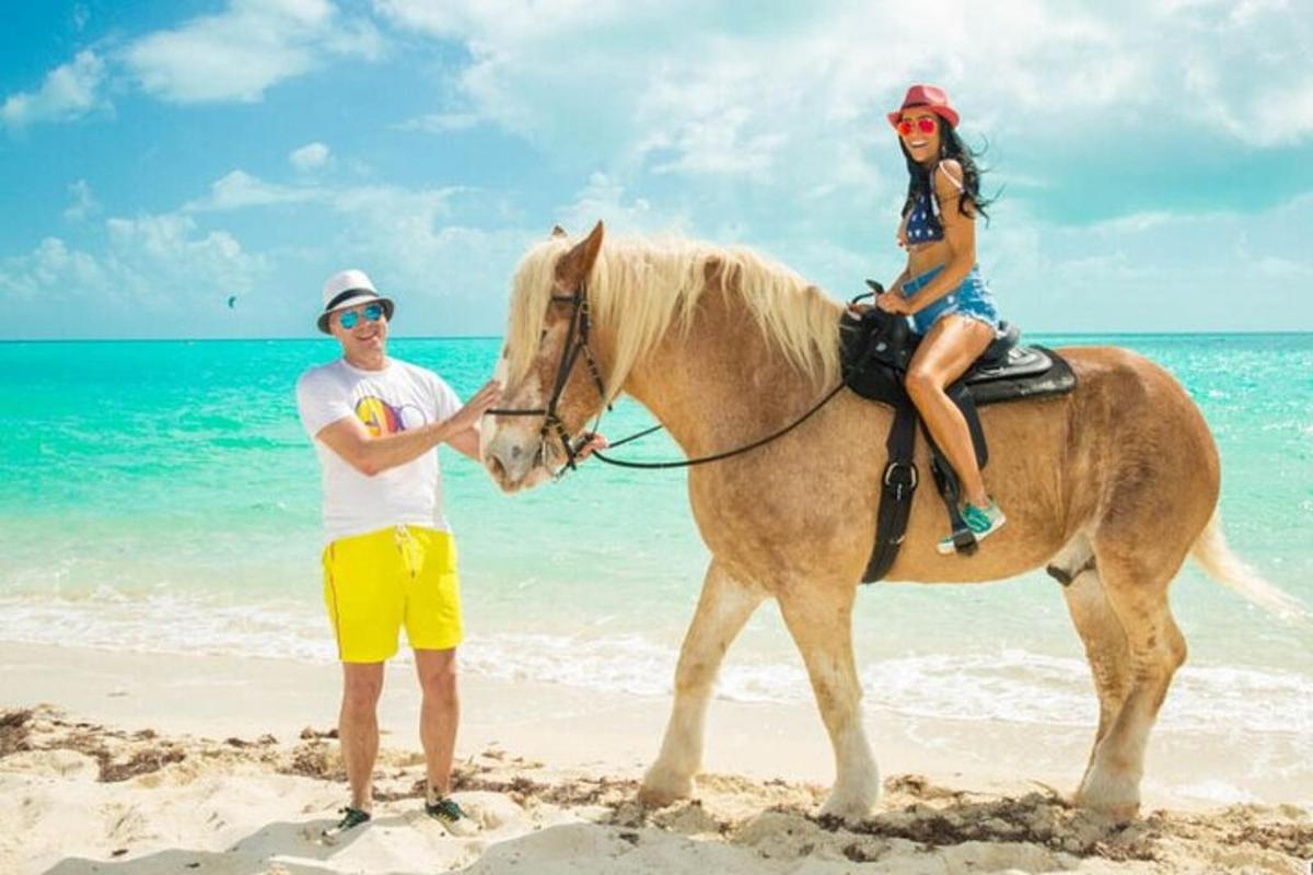een man en een vrouw rijden op een paard op het strand