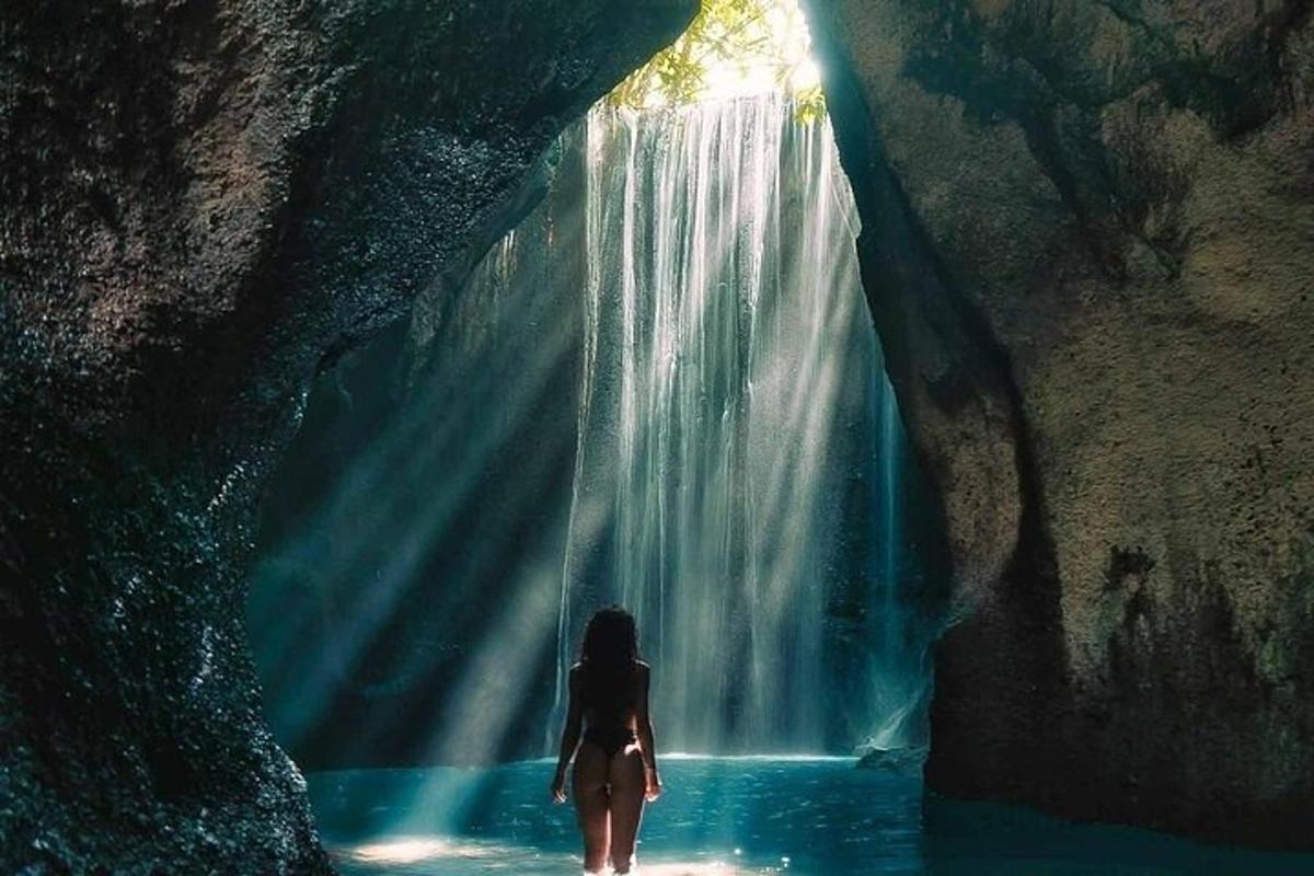 seorang wanita berdiri di dalam air berhampiran air terjun