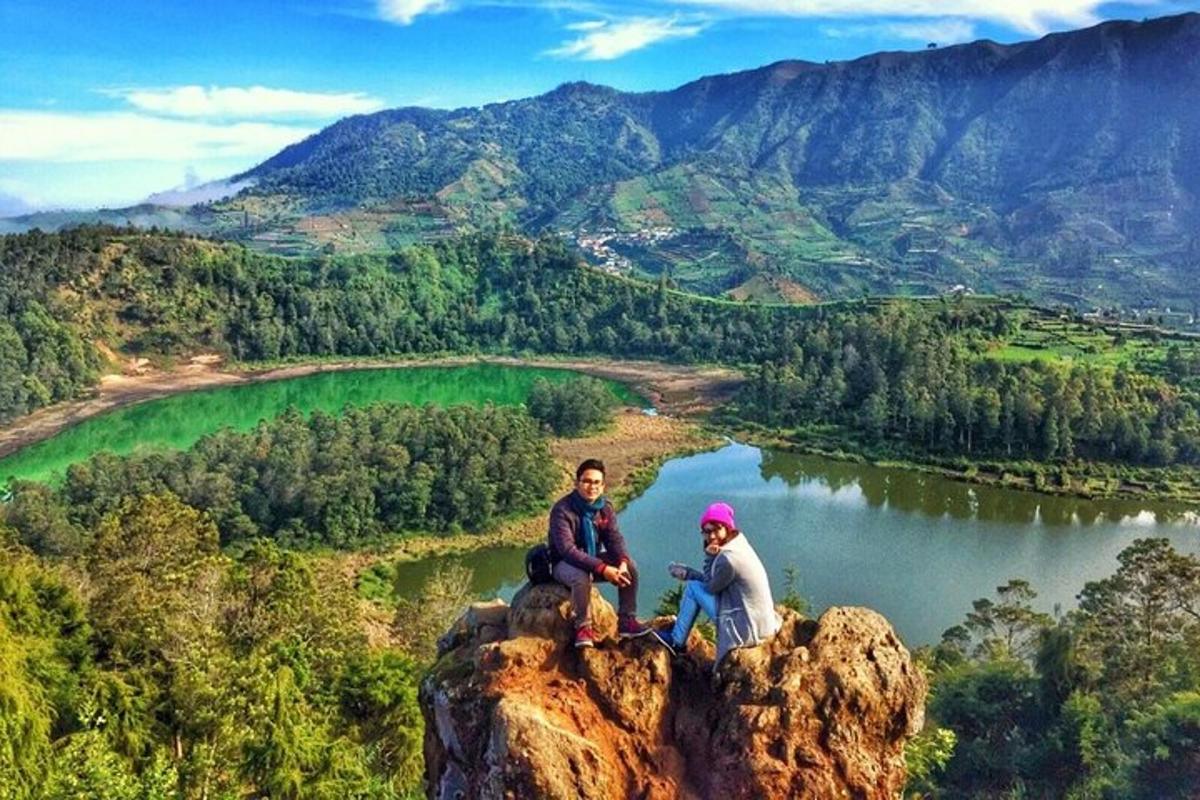 Dos personas sentadas en lo alto de una roca con vistas a un lago.