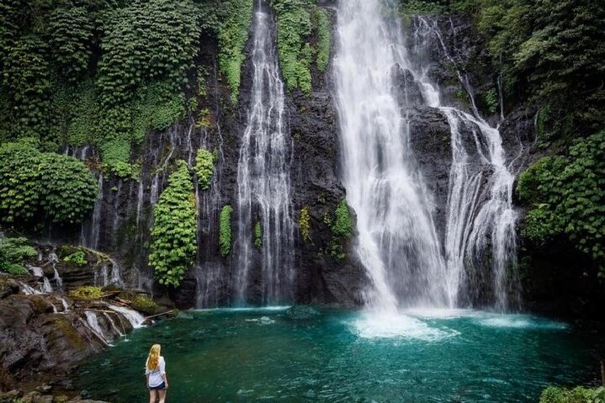 kona stendur í vatnspolli fyrir framan foss