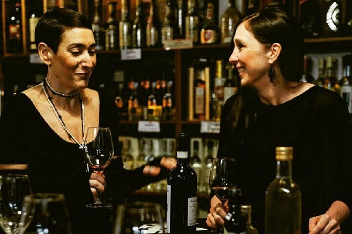 Dos mujeres de pie en un bar con copas de vino