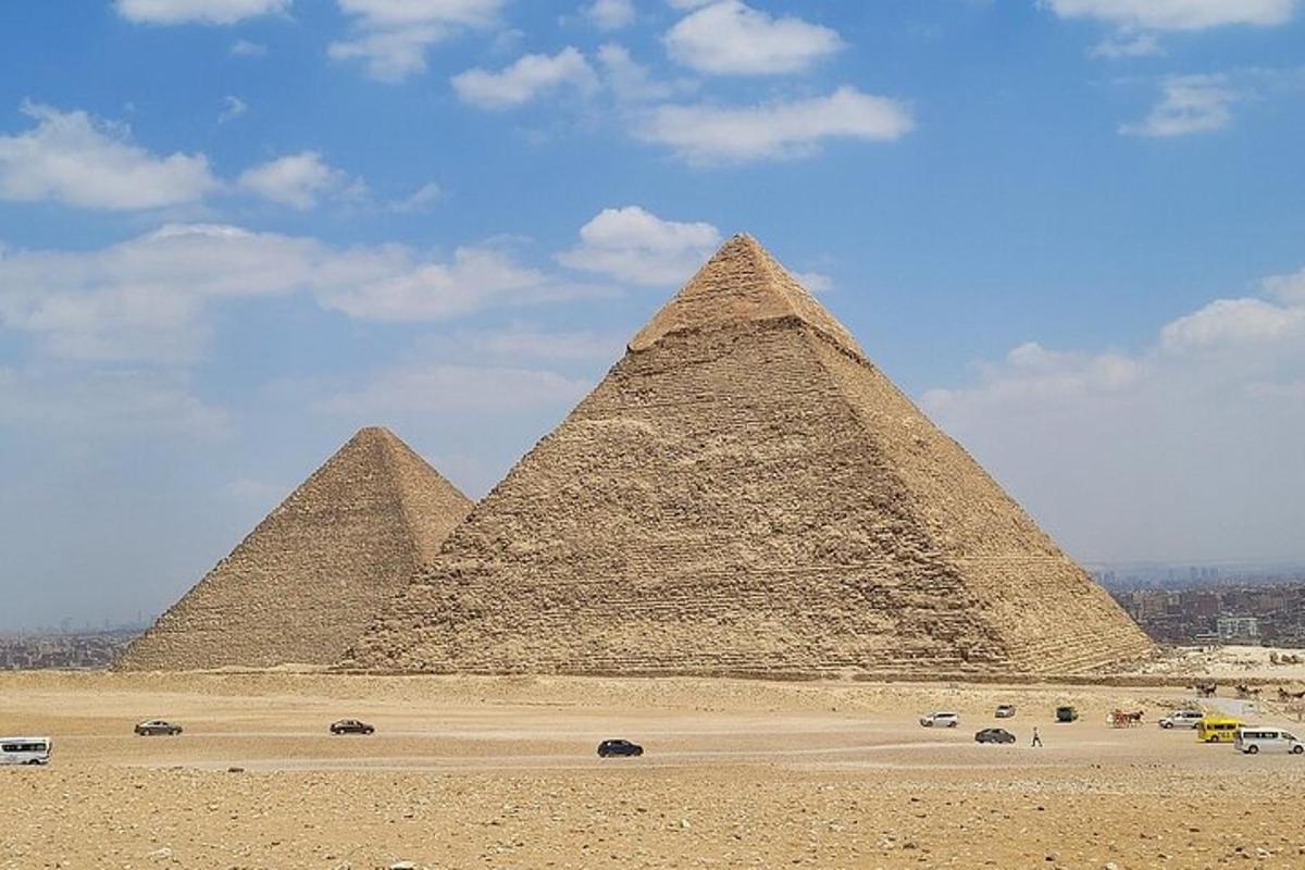 Skupina pyramid v poušti s auty před nimi