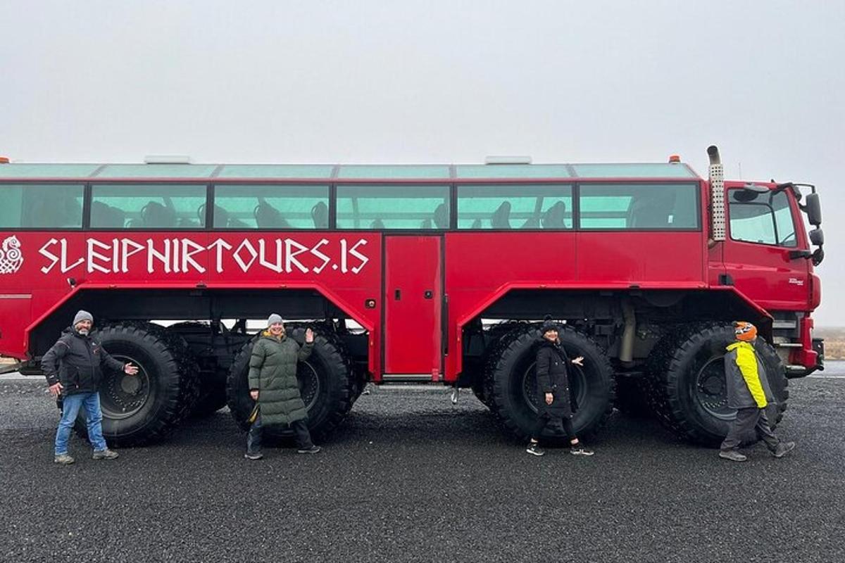 skupina lidí stojící vedle velkého červeného autobusu