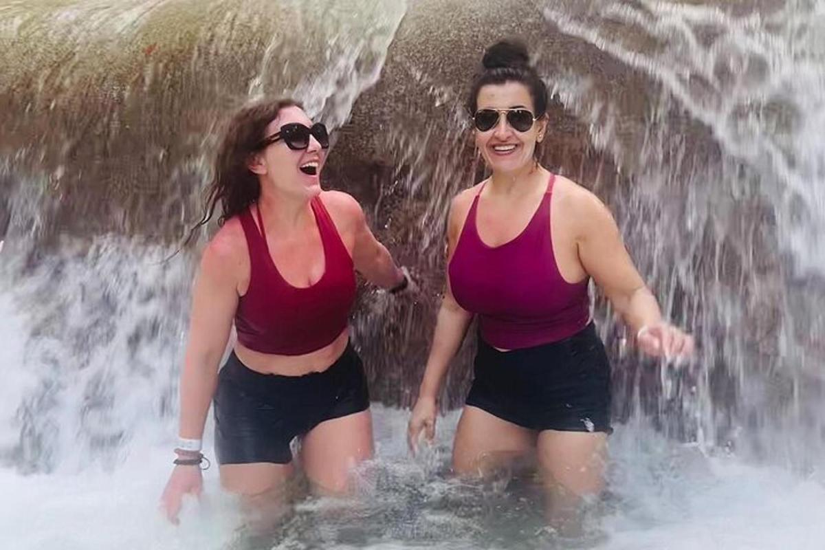 duas mulheres na água em frente a uma cachoeira