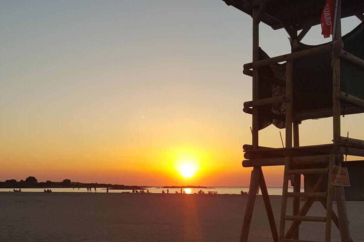 un tramonto sulla spiaggia con una sedia da bagnino