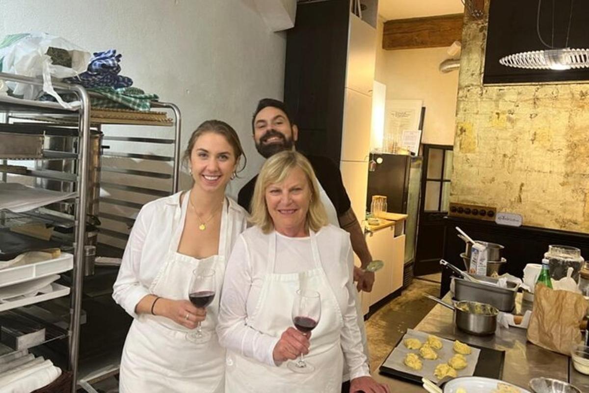 two women and a man standing in a kitchen holding wine glasses