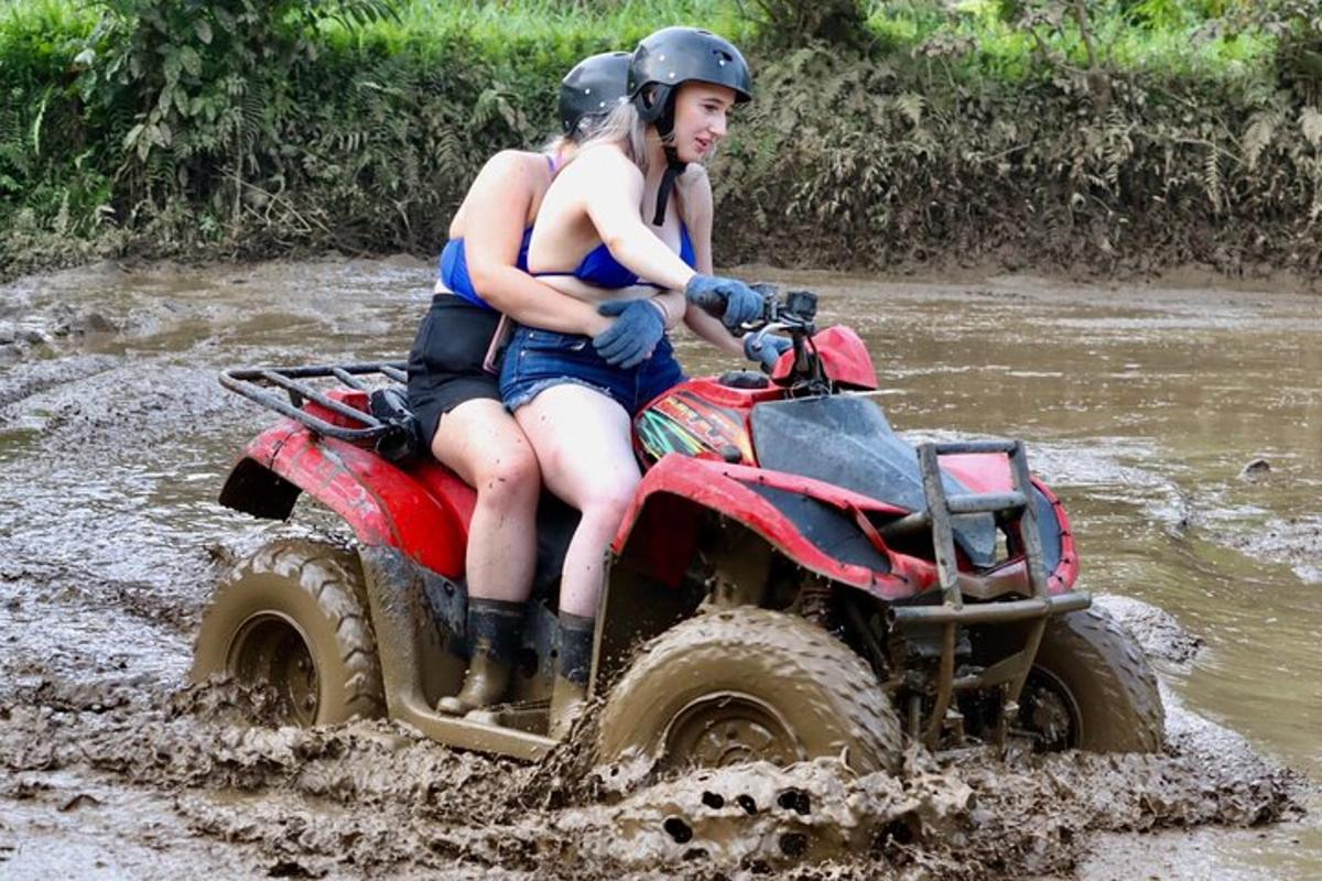 two people riding on a four wheeler through the mud