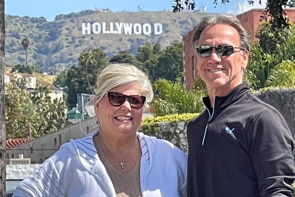 seorang lelaki dan wanita berdiri di hadapan papan tanda hollywood