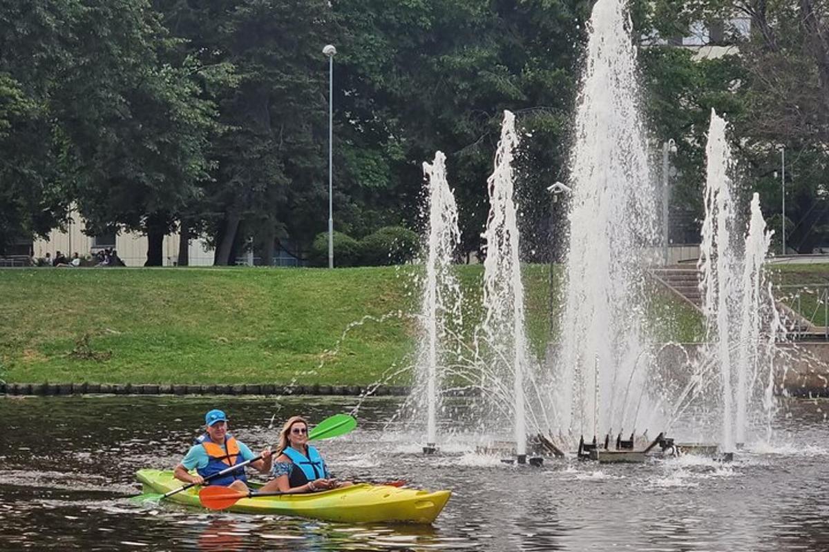 két ember lovagol egy tutajon egy szökőkút előtt