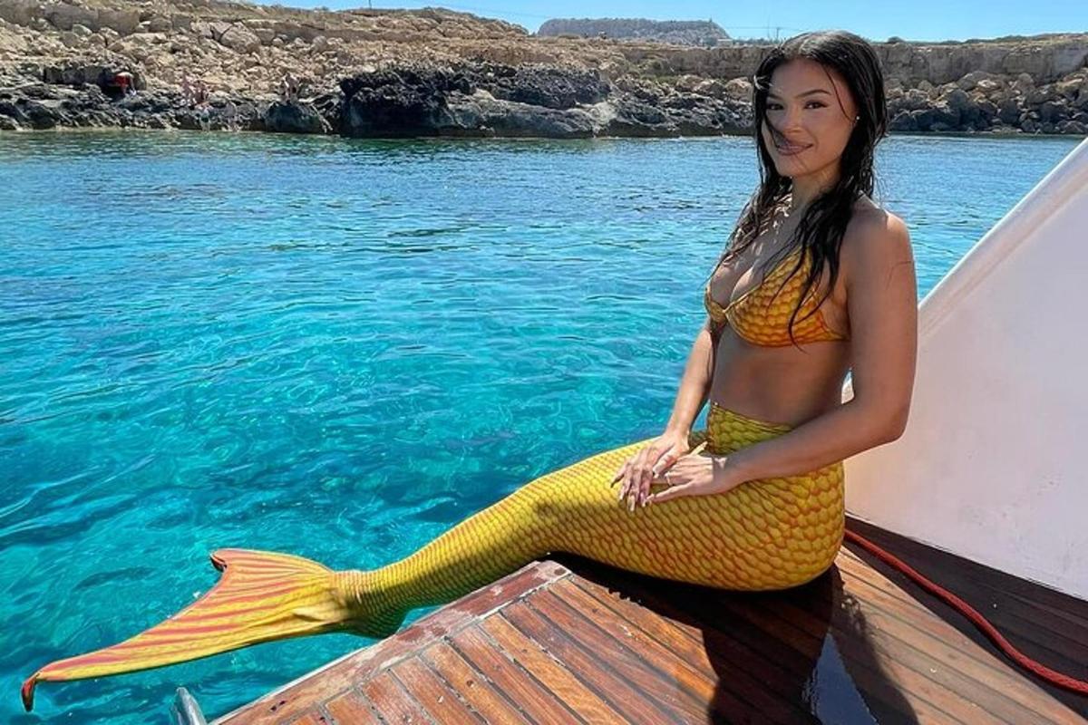 kona sitjandi á báti með gulan hafmeyjarhala
