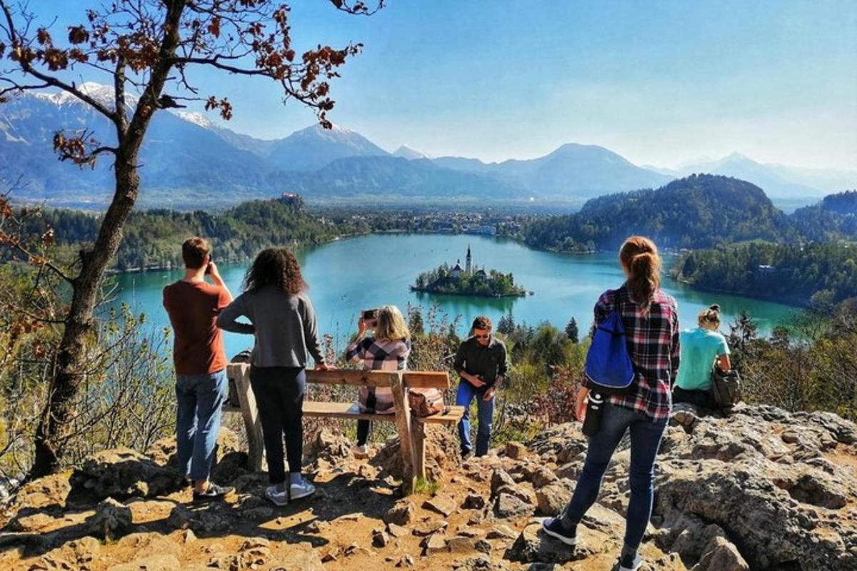 eine Gruppe von Menschen steht um eine Bank herum und blickt auf einen See