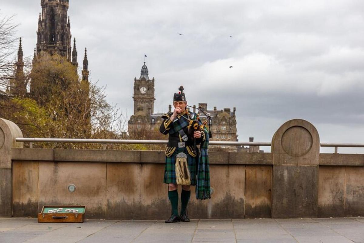 un home amb un kilt dret sobre un pont amb una torre de rellotge